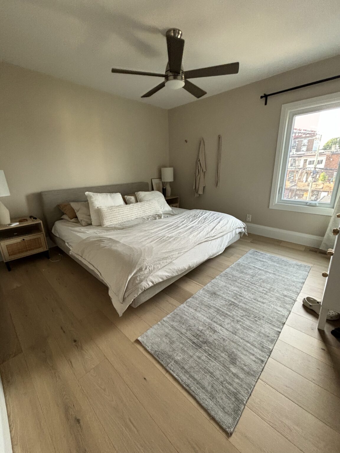 Spacious master bedroom with light wooden flooring, a modern ceiling fan, and a cozy bed setup.