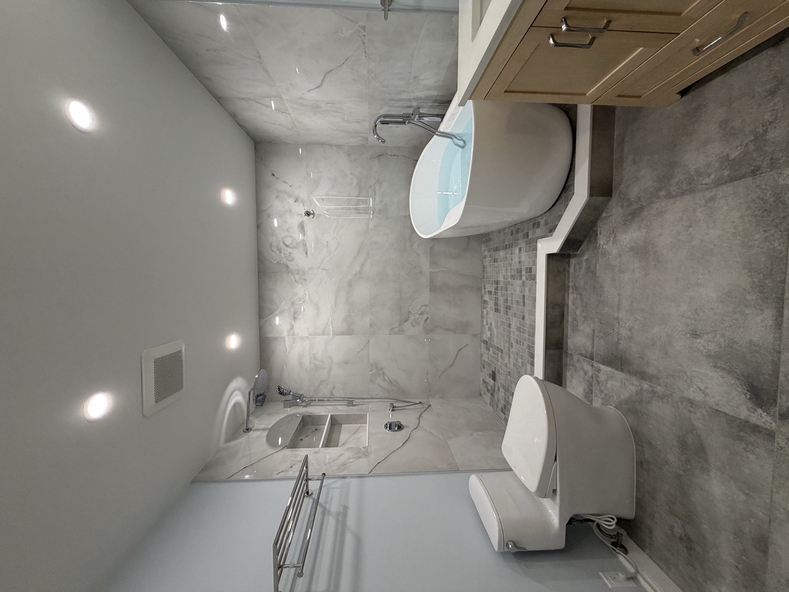 Finished five-piece Mississauga condo bathroom with a podium-mounted freestanding tub, walk-in shower, smart toilet, and heated towel rack in marble-look porcelain tile