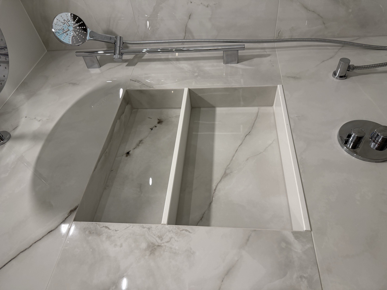 Close-up of a two-shelf custom recessed shower niche built into large-format marble-look porcelain tile with clean waterproofed edges