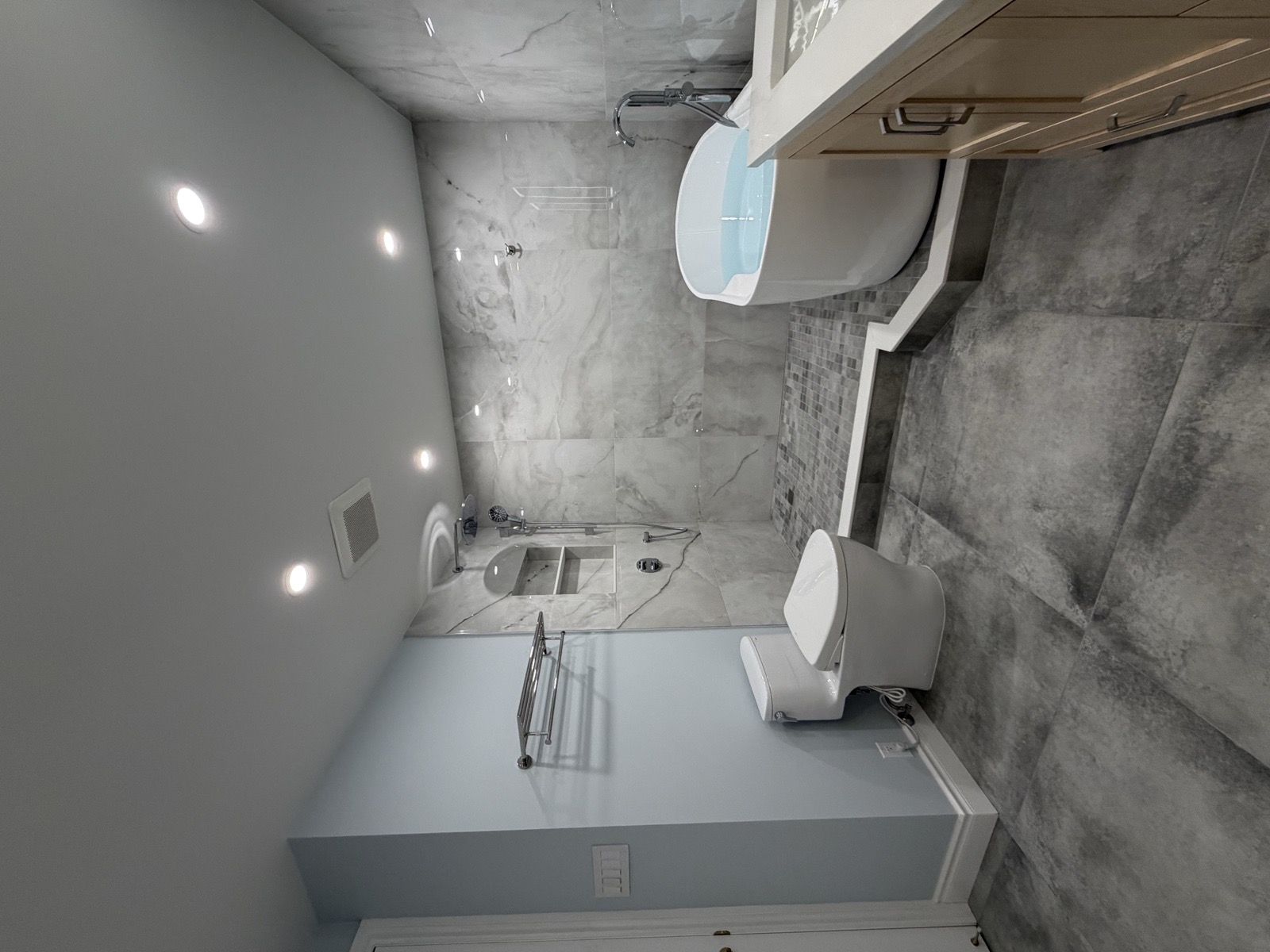 Freestanding tub and curb walk-in shower combined on a custom podium with a recessed niche, heated towel rack, and marble-look porcelain tile