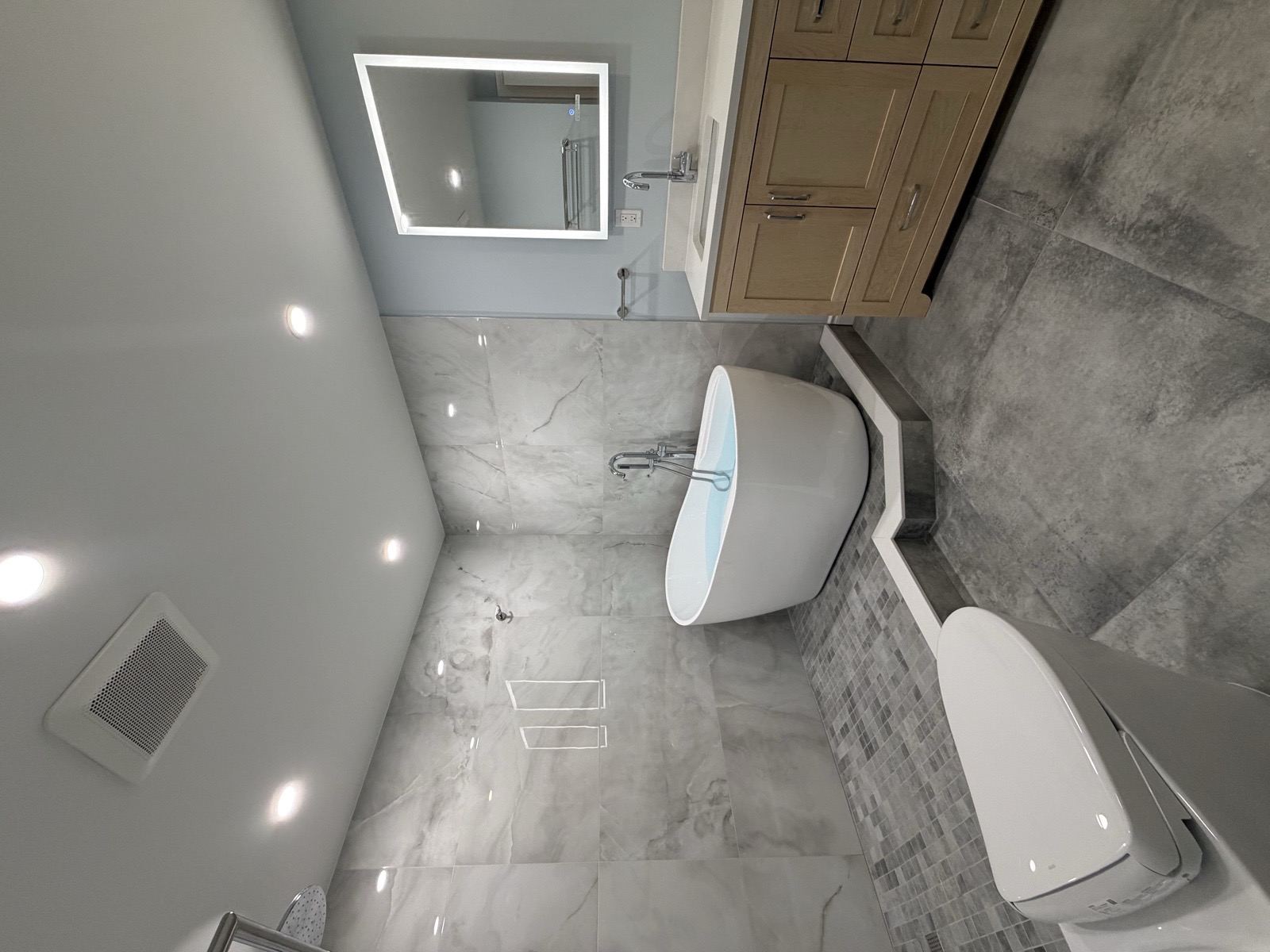 Smart toilet in the foreground with a freestanding tub on a tiled podium and a vanity with LED mirror behind in a renovated Mississauga condo bathroom