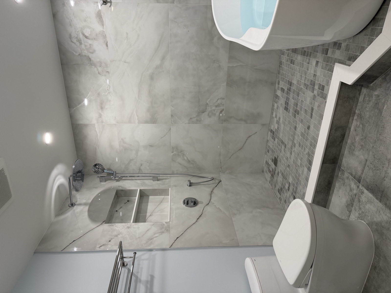 Walk-in shower with mosaic-tile floor on a raised podium next to a freestanding tub and a smart toilet in a renovated Mississauga condo bathroom